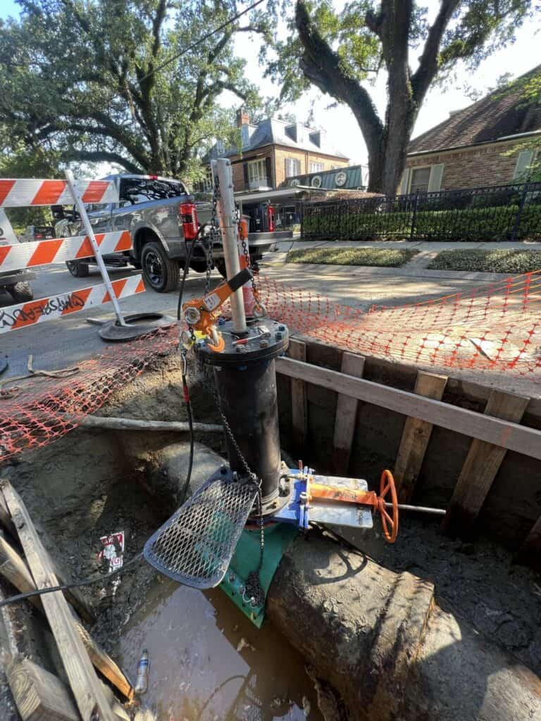 A pipeline services valve with an orange handle installed in an excavated trench in a residential neighborhood.