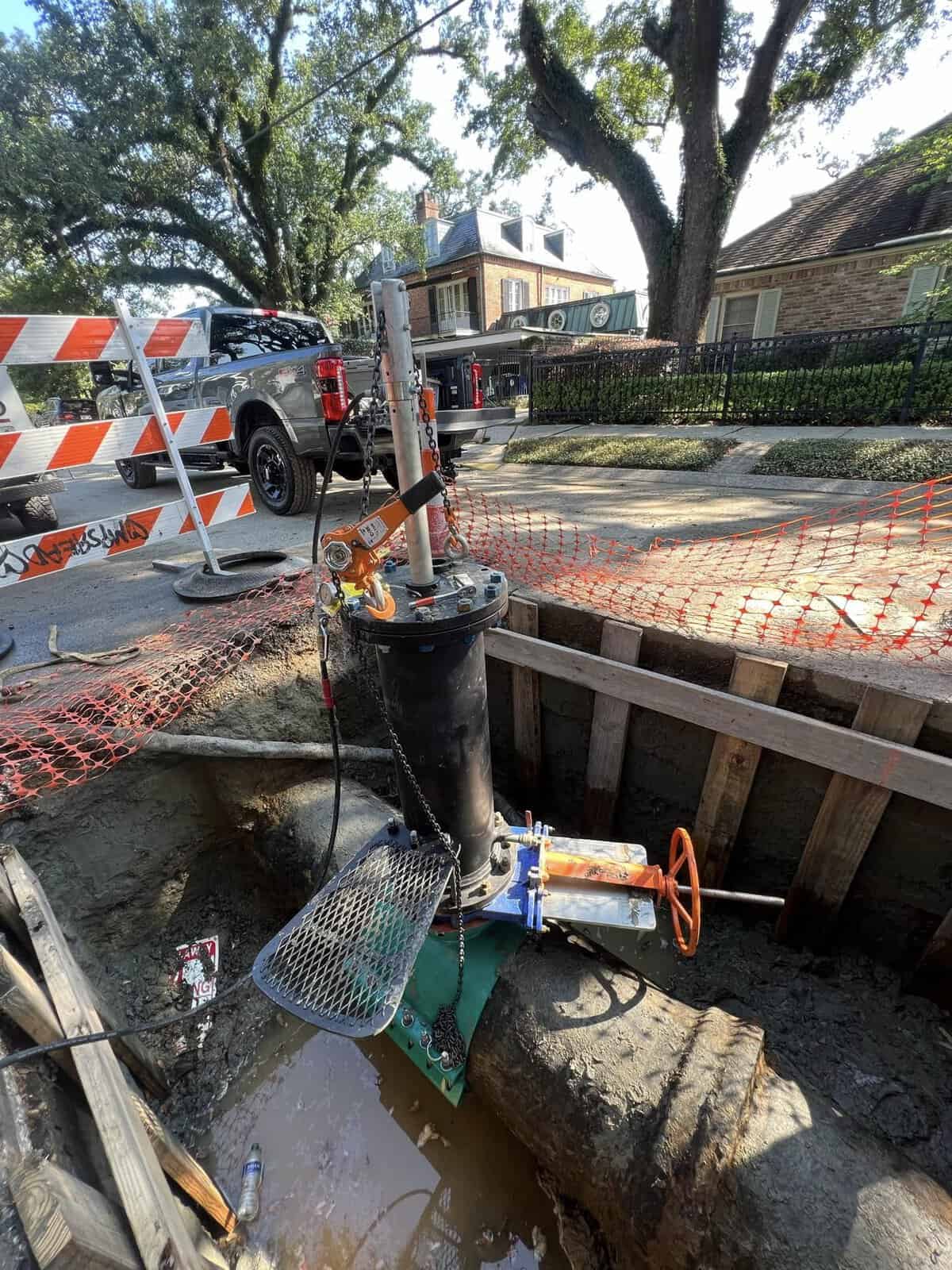 A pipeline services valve with an orange handle installed in an excavated trench in a residential neighborhood.